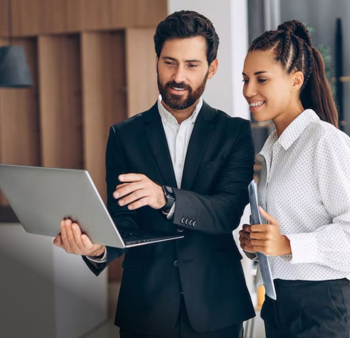 Channel partner and client smiling while collaborating over a laptop, discussing Hexnode at the office.