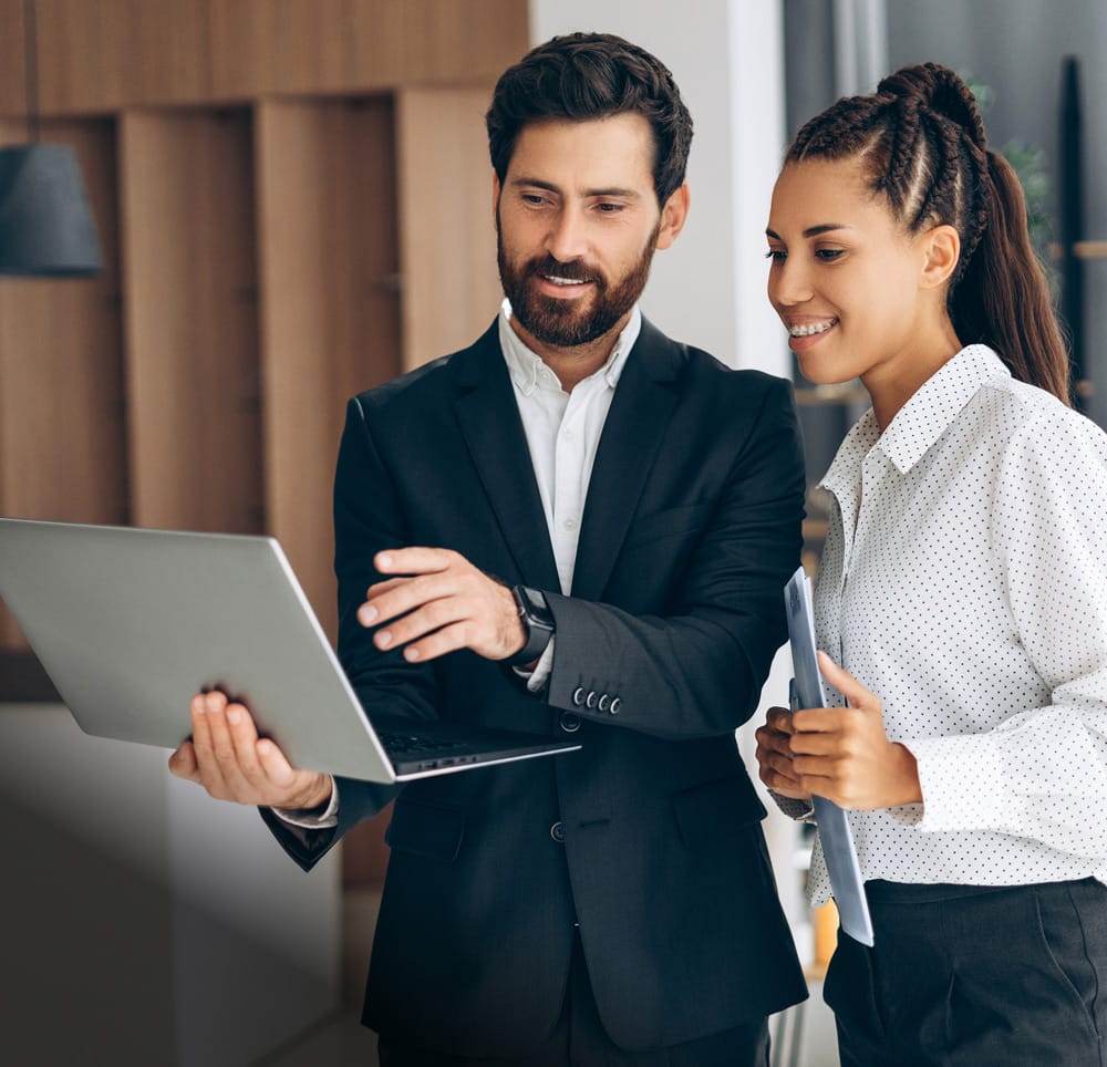 Channel partner and client smiling while collaborating over a laptop, discussing Hexnode at the office.